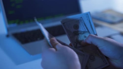 Hands Counting Cash Next to Open Laptop