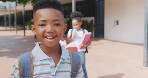 Video portrait of smiling african american schoolboy with schoolbag outside school, with copy space