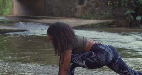 A girl engaging in yoga by a lush riverbank on a warm Caribbean afternoon.