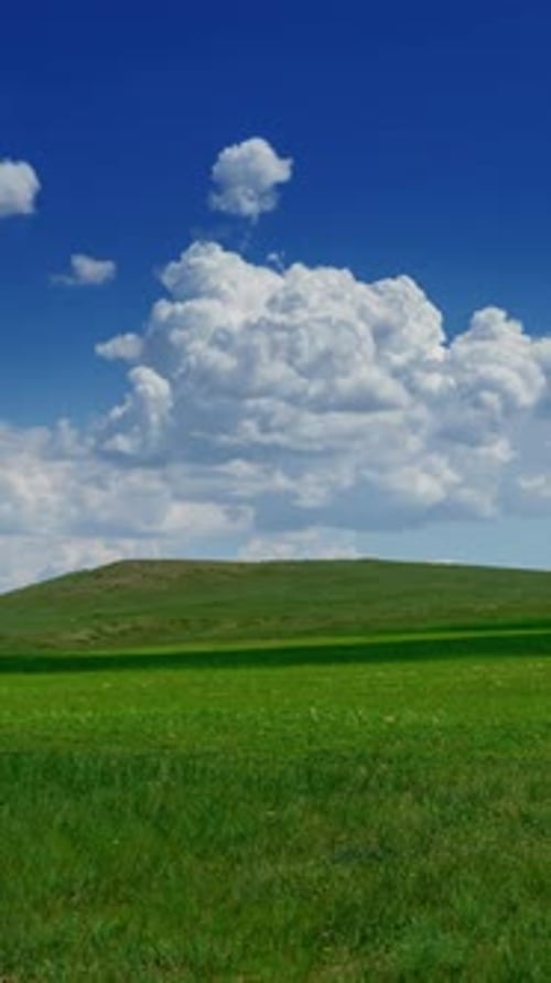 Green hill with grass under cloudy sky, timelapse