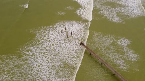 Vista aérea do cais que se estende até o oceano com água verde acastanhada