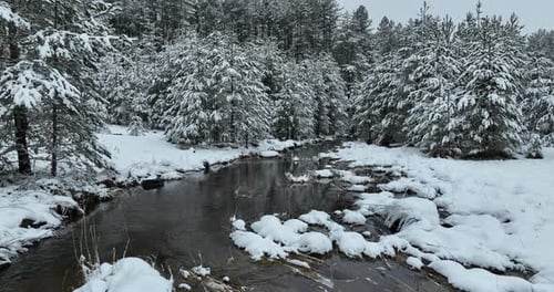 Eine Luftaufnahme eines gefrorenen Flusses, der durch schneebedeckte Wälder fließt, an einem bewölkten Sonnenuntergangshimmel