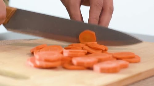 Close-up of Woman's hand cutting a carrot.Side frame, focused on the knife blade.