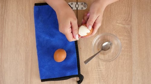 Woman Peeling Hard Boiled Egg on Wooden Table
