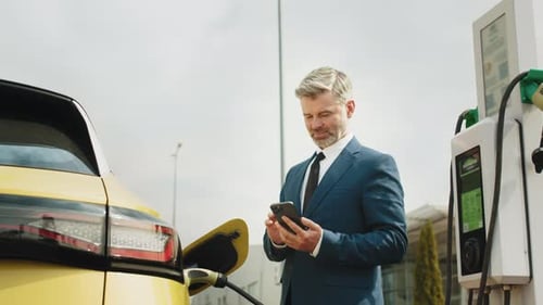 Man Using Phone at Electric Vehicle Charging Station