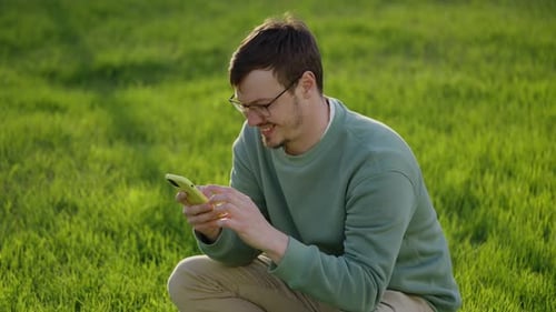 Man Crouching in Field Using Mobile Phone