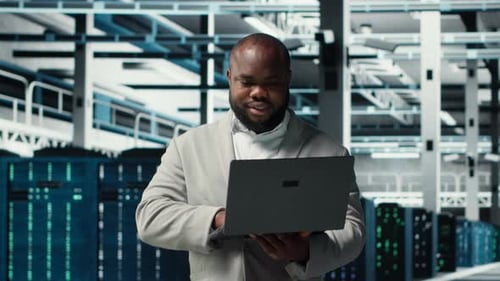Smiling Engineer in Data Center Managing Software Using Laptop