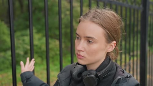 Young Woman Stands by Gate in City Park