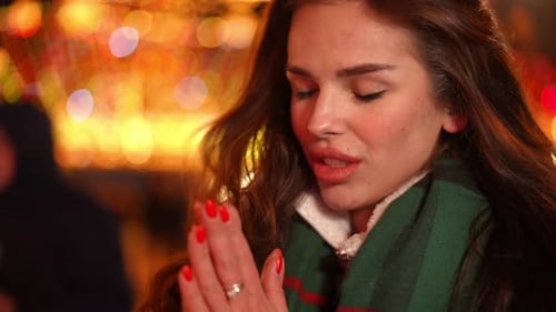 Closeup Portrait of Young Slim Caucasian Woman Blowing on Palms Warming Hands Standing Outdoors on