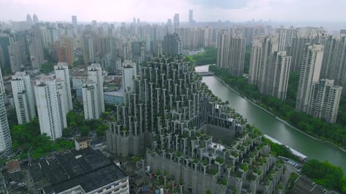 Aerial Concrete Terraced Building with Greenery Surrounded By Residential Skyscrapers and a Winding