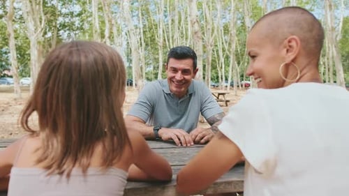 Family mom and dad sitting on bench in city park with daughter talking and smiling
