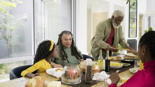 Diverse multigenerational family passing dishes to serve salad and corn at table prepping dinner
