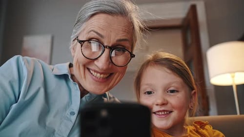 Closeup Portrait of Happy Loving Grandmother and Her Granddaughter Using Smartphone Watch Cartoons