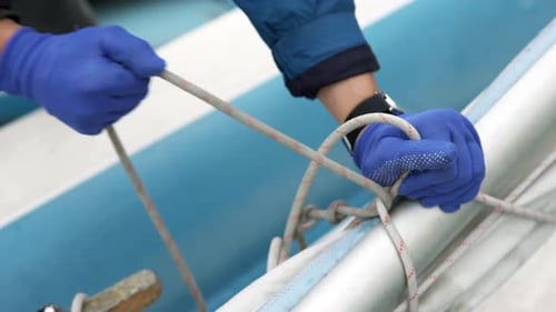 The yachtsman lowers the mast and furls the sail and tightens the knots on the sailboat.