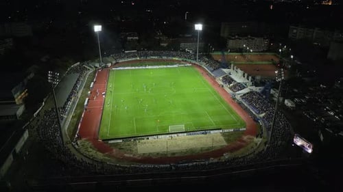 Drone Footage Capturing a Night Football Match in a Brightly Lit Stadium Spectators Fill the Stands