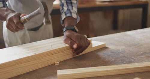 Mid section of african american male carpenter hammering nails into the wood at a carpentry shop