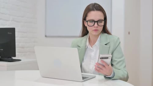 Woman Using Phone and Laptop in Office