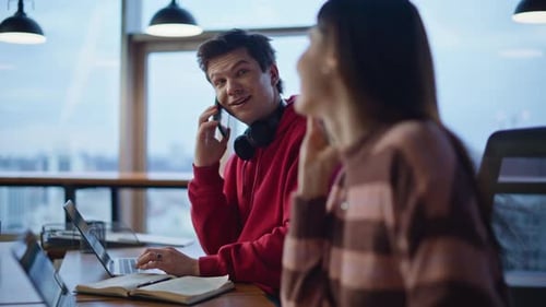 Two Consultants Talking Smartphones Entering Orders in Laptops at Office Closeup