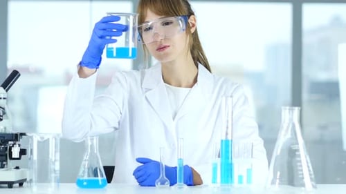 Female Scientist Examines Beaker with Blue Liquid