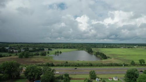 A beautiful still lake is visible from a drone hovering over a busy highway with moving vehicles.