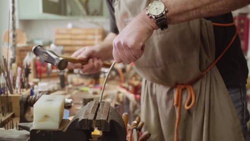 Instrument maker hammering metal bar into shape inside vice. The piece of metal it later used for fo