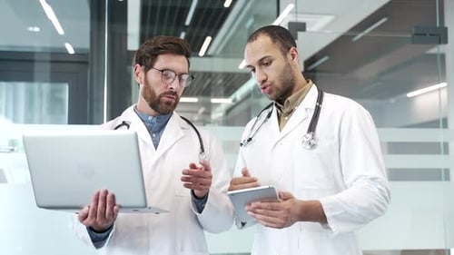 Two doctors talking over laptop and tablet standing in hospital office. Medical professionals