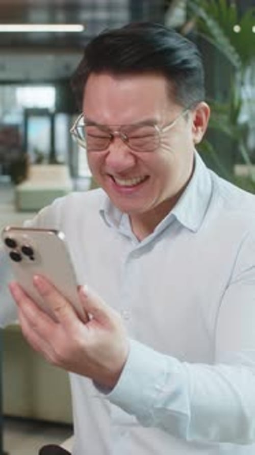 Happy Amazed Businessman Using Smartphone Shocked By Sudden Victory Lottery Win in Office Lobby