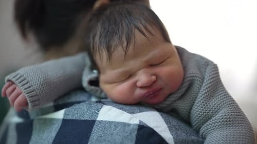 Close-up of a newborn baby resting on the mother’s shoulder after breastfeeding, highlighting the