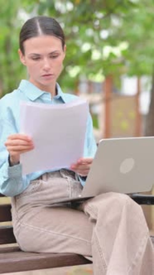 Woman Works on Laptop and Reads Paper