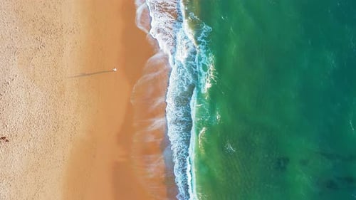 Aerial View of Beach with Rolling Waves Creating White Foam on Sunny Day