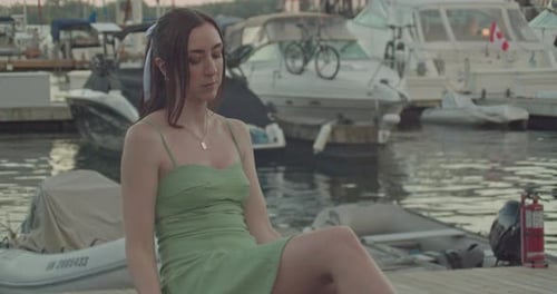 Weiße brünette Frau im grünen Sommerkleid mit weißer Haarschleife, sitzt am Hafen