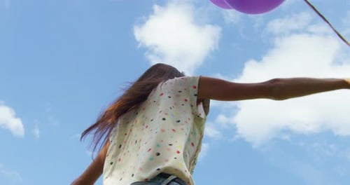 Woman Jumping with Balloons Against Blue Sky