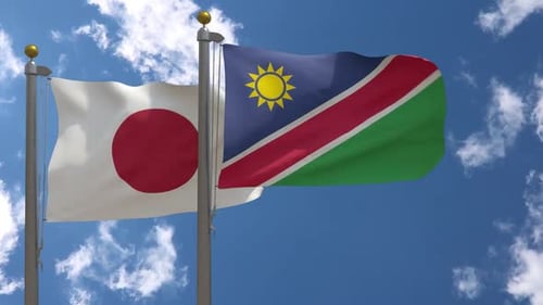 Japan And Namibia Flags Waving In Blue Sky With Clouds