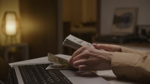 Hands Counting Money Next to Laptop
