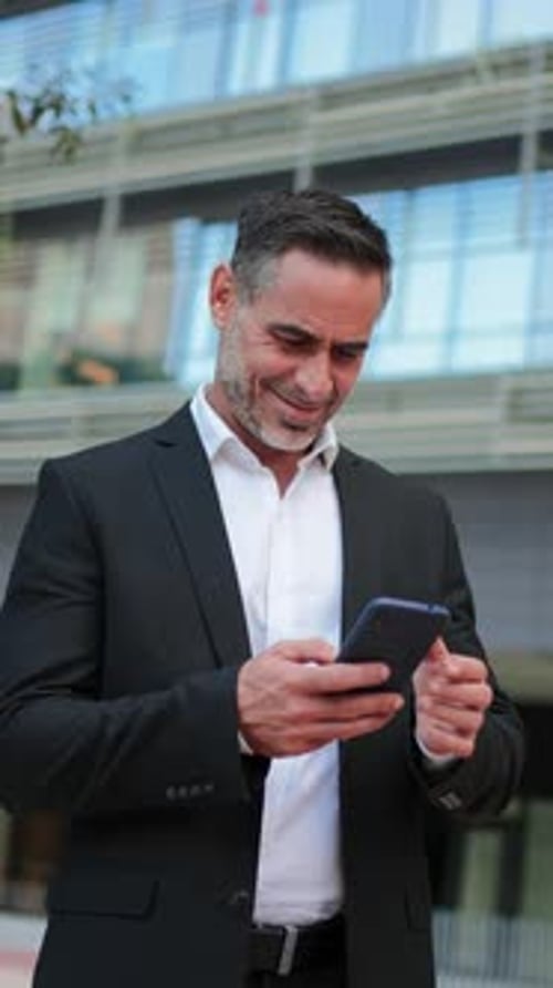 Confident Businessman Using Smartphone for Work While Standing Outdoors in a Stylish Black Suit