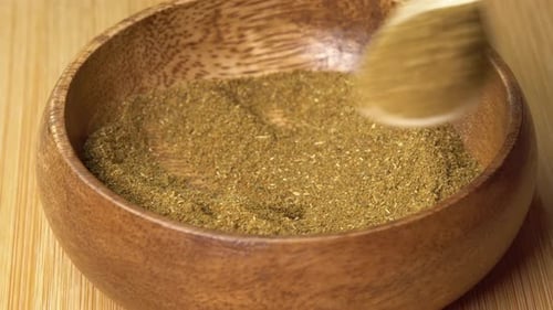 La cuchara recoge las especias de lúpulo Khmeli suneli de un tazón de madera y gira sobre una tabla de madera.