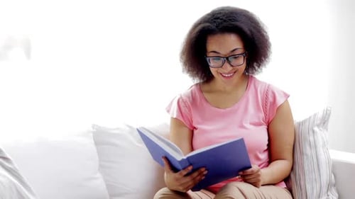 Leisure, Literature And People Concept - Smiling African American Young Woman In Eyeglasses Readi...