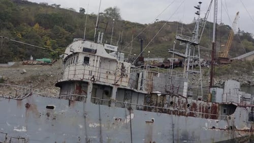Rostgraues, halb untergetauchtes Schiffswrack, das an einem bewölkten, bewölkten Tag in Küstennähe vor Anker lag. Langsamer Aufstieg sh