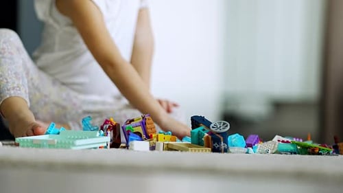 Close Up View of Little Girl Playing with Small Constructor Toy on the Floor in Home Living Room