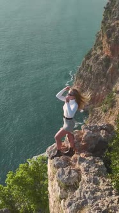 Vertical Video Elegant Model Posing Fearlessly on a Cliff Overlooking the Vast Mediterranean