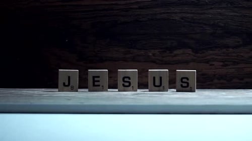 The word "JESUS" spelled out in wooden letters with overhead fluttering lighting