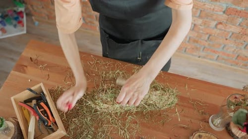 Woman crafting floral wreath at wooden table, top view