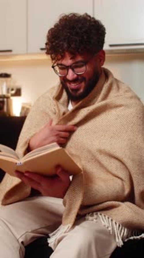 Man Reading Book Wrapped in Blanket on Couch