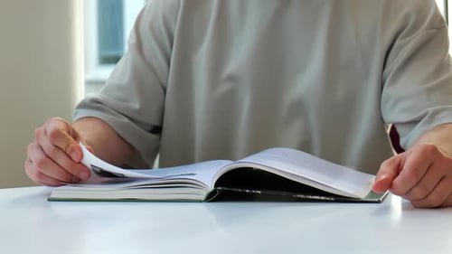 Man reading book at table indoors, turning pages