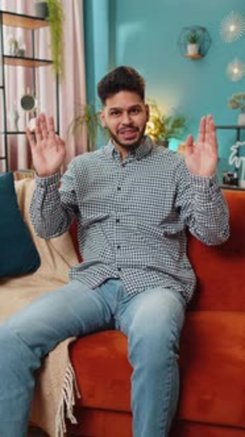 Young Adult Waving from Couch in Home Interior