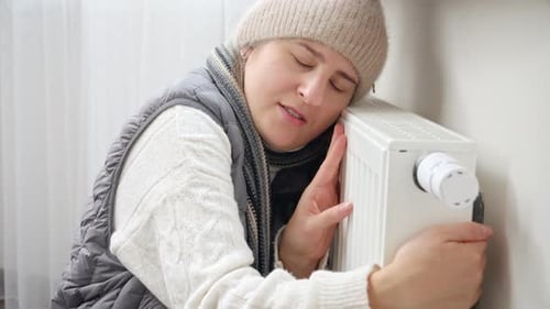 Woman Warming Up Against Radiator Indoors