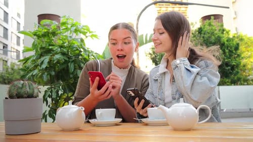 Young Women Enjoying Tea and Phones at Cafe