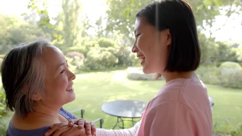 Smiling senior asian woman receiving physical therapy from caregiver in garden