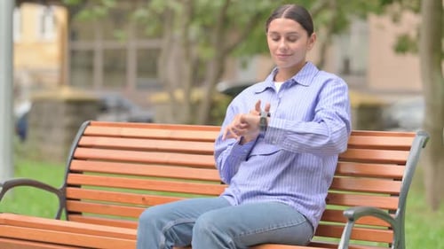 Young Woman Using Smartwatch While Sitting on Bench