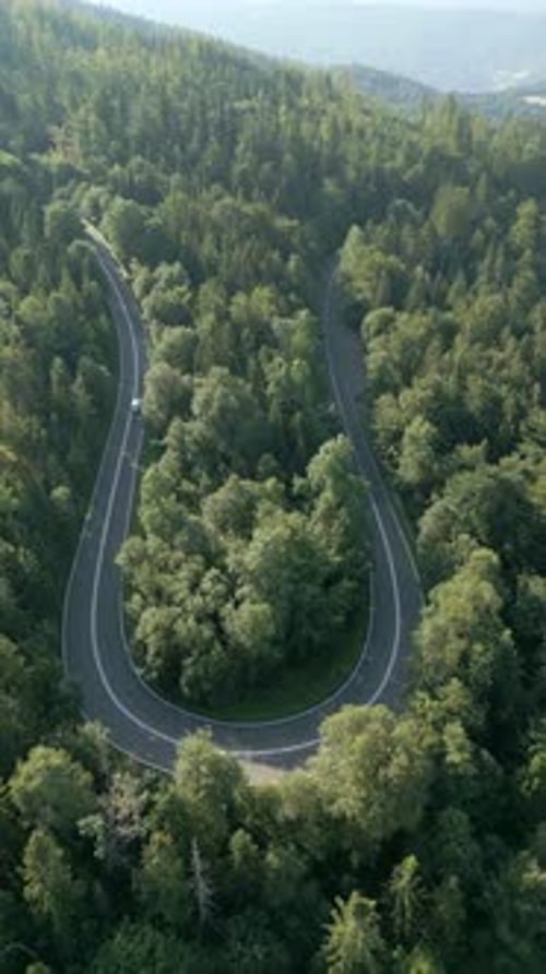 Aerial View Of A Car Driving On A Winding Road Through Summer Mountain Forest